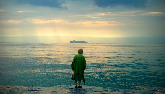 пожилая женщина в одиночестве стоит на берегу